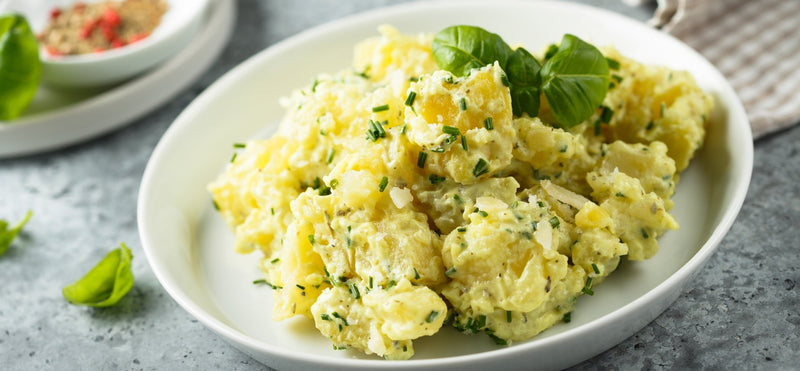 Creamy potato salad with herbs in a white bowl