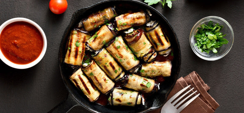 Grilled eggplant cannelloni rolls in a skillet with tomato sauce and parsley