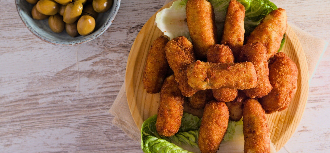 Golden ham croquettes on a wooden plate with olives and lettuce