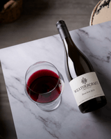 A bottle of Weathercraft Vineyard Pinot Noir 2021 wine and a glass of red wine on a white marble surface.