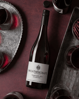 A bottle of Weathercraft La Tordera Tempranillo 2022 red wine, styled on a dark burgundy surface with galvanized trays and glasses of red wine.